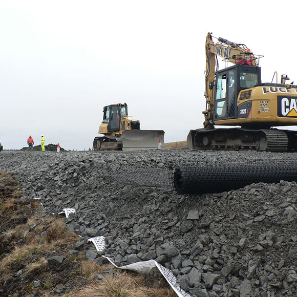 Two construction vehicles and construction workers constructing a unsurfaced road using Tensar's geogrids 
